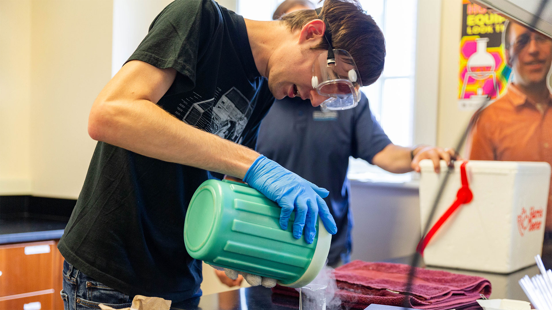 A student wearing lab goggles pours liquid nitrogen into a beaker